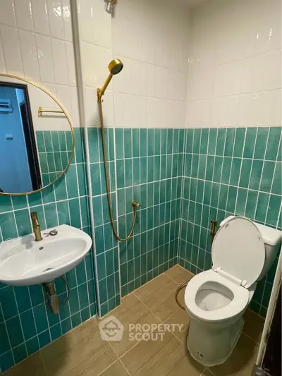 Modern bathroom with teal tiles and gold fixtures, featuring a round mirror and compact design.