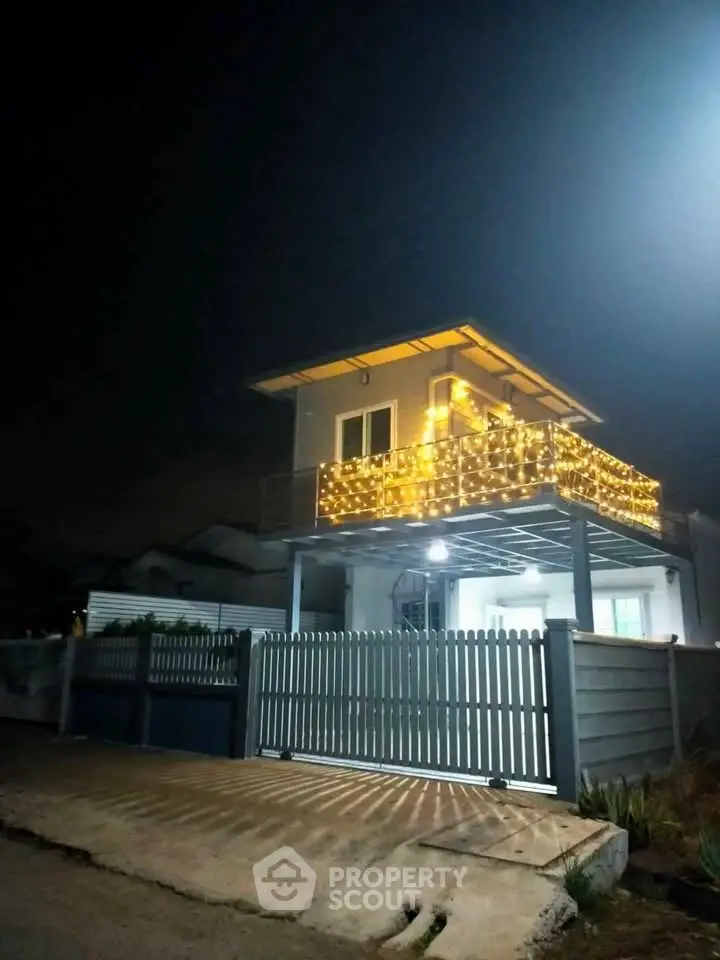 Charming two-story house with illuminated balcony at night, perfect for cozy evenings.