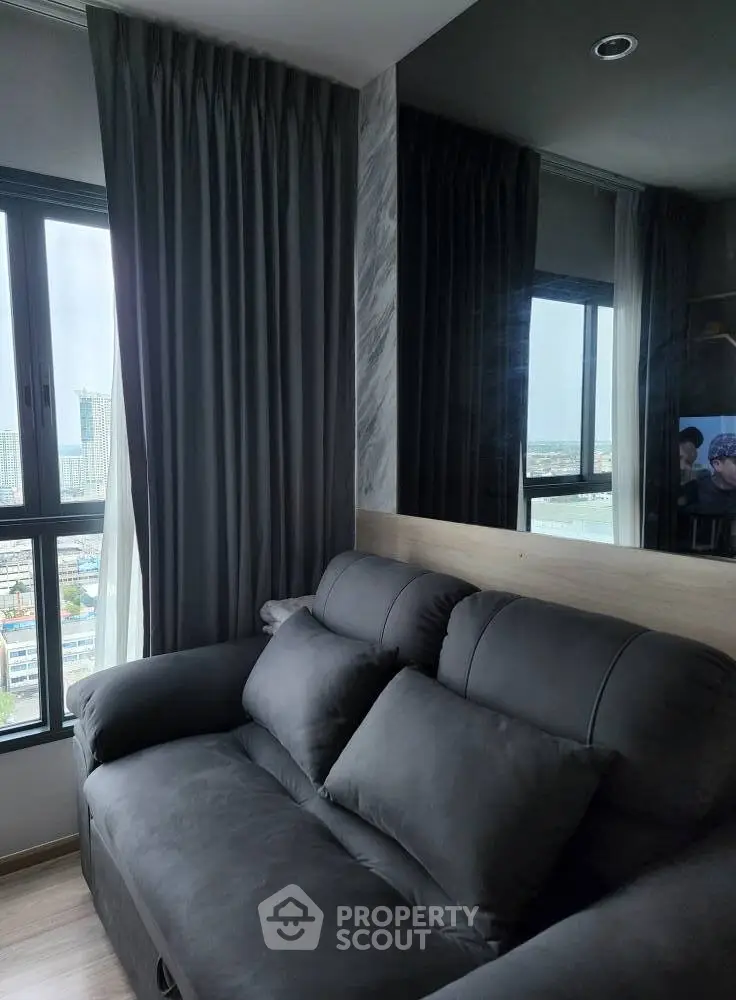 Modern living room with sleek black sofa and large windows offering city views, perfect for urban living.