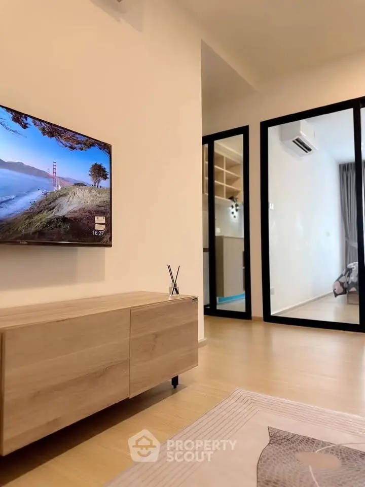 Modern living room with sleek wooden furniture and wall-mounted TV, featuring a glimpse into a stylish bedroom.