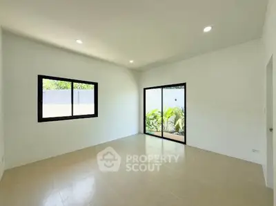 Spacious empty room with large windows and sliding glass door to garden view.