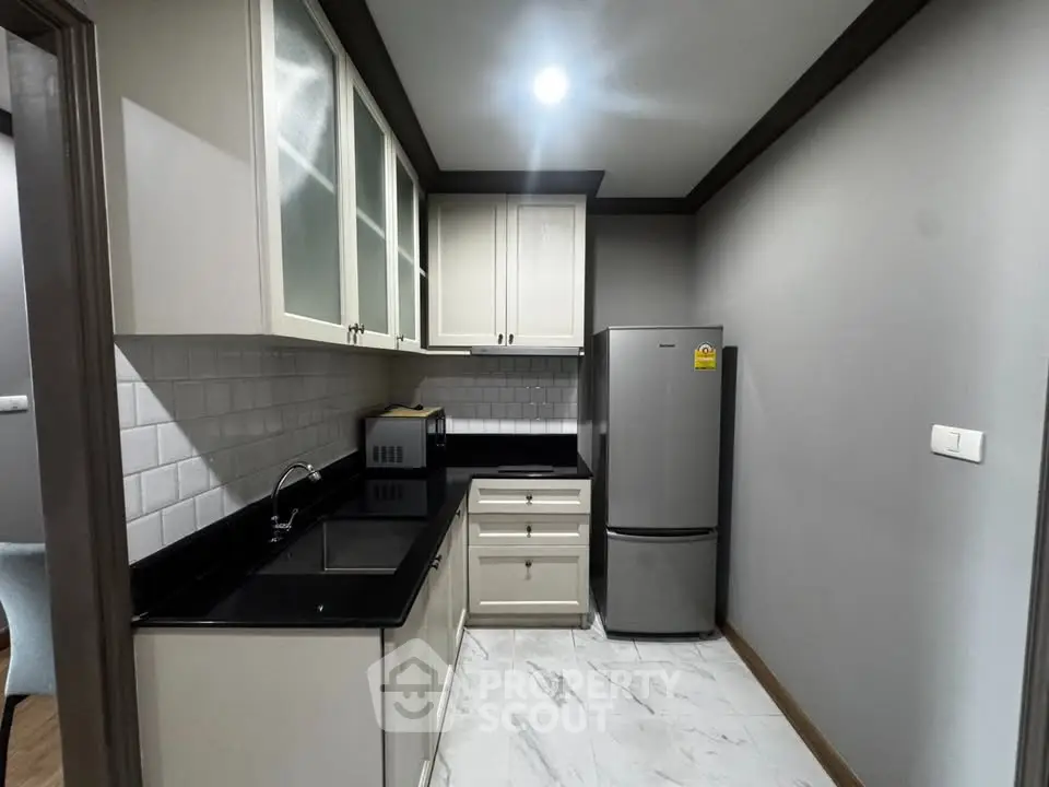 Modern kitchen with sleek black countertops and stainless steel fridge in a stylish apartment.