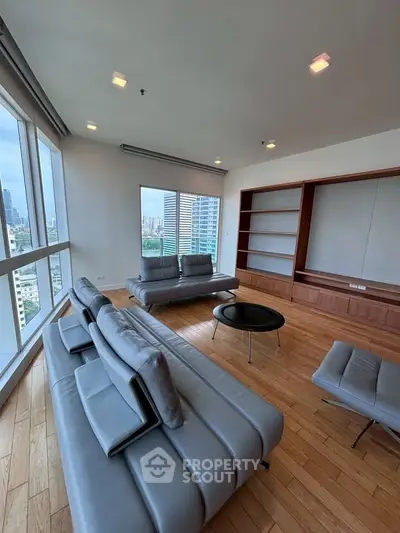 Spacious modern living room with city view, featuring sleek leather sofas and wooden flooring.