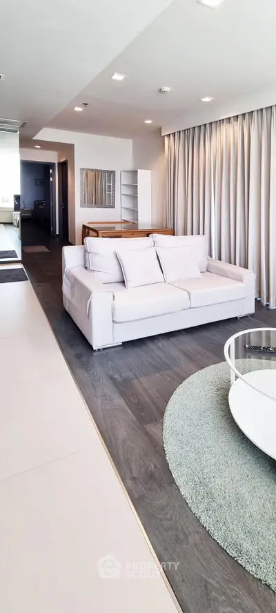 Modern living room with sleek white sofa, stylish rug, and floor-to-ceiling curtains in a contemporary apartment.