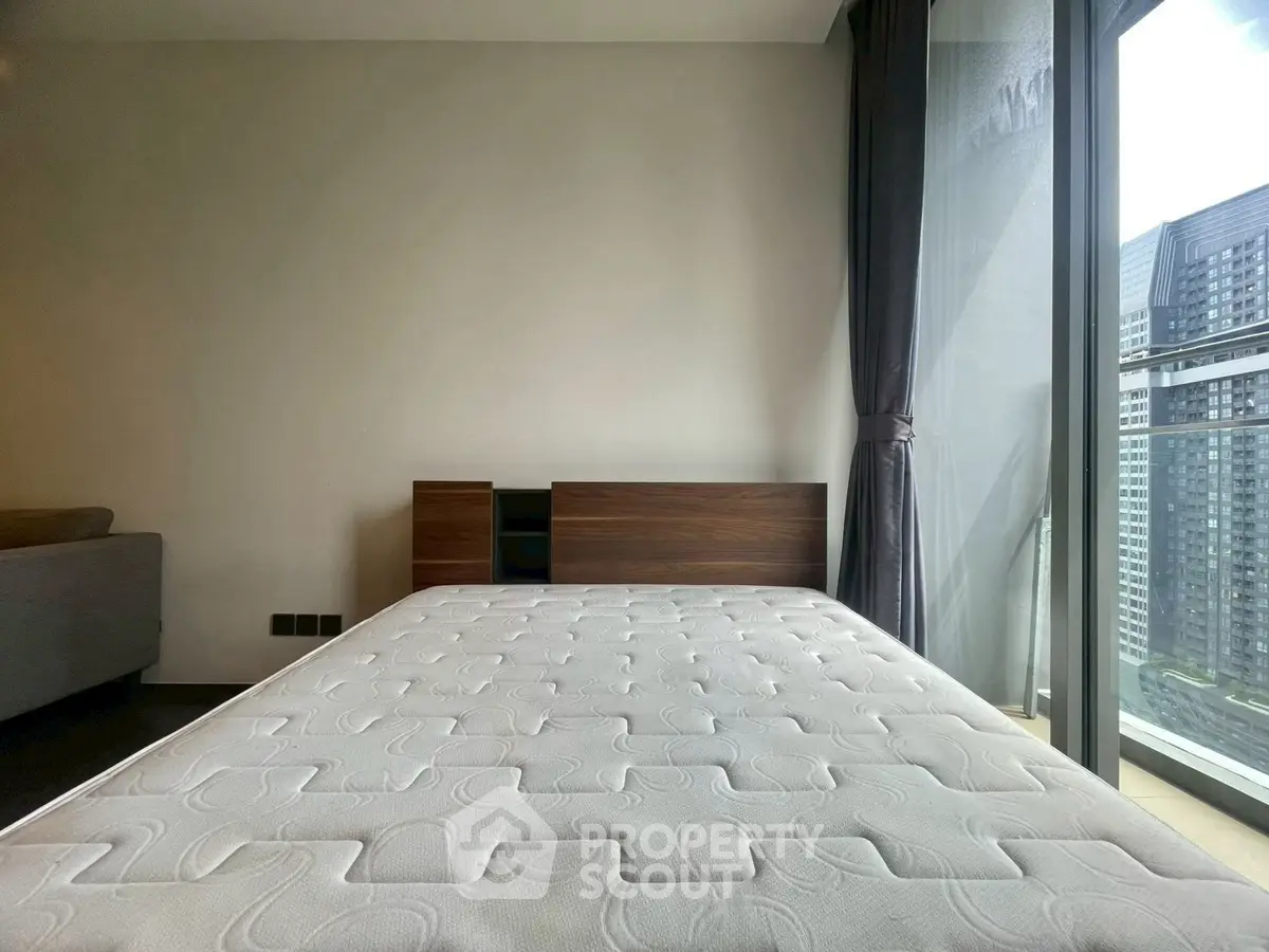 Modern bedroom with large window and city view, featuring a minimalist design and comfortable mattress.