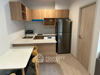 Modern kitchen with wooden cabinets, stainless steel fridge, and dining area in cozy apartment.