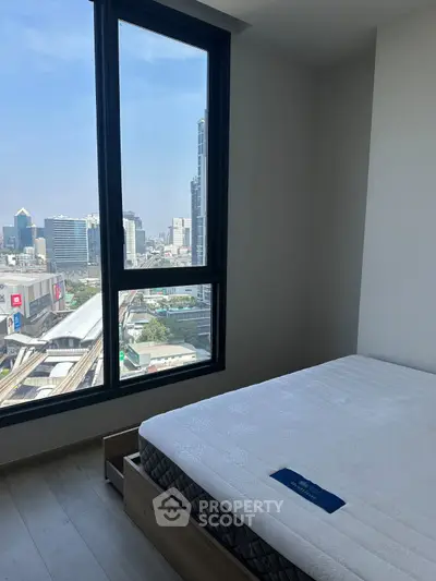 Modern bedroom with city view, featuring large window and comfortable bed, perfect for urban living.