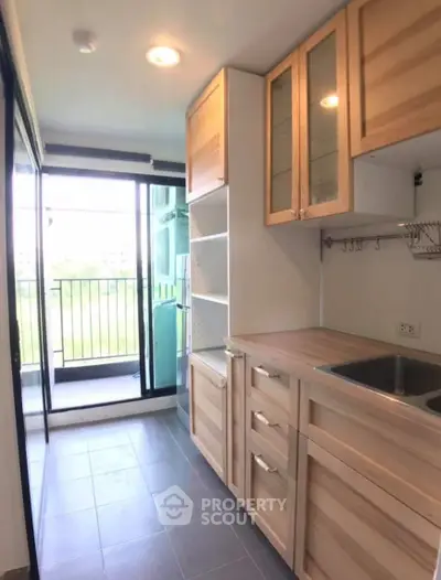 Modern kitchen with wooden cabinets and balcony access in a bright apartment.