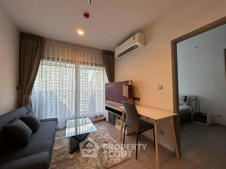 Modern living room with stylish furniture and large window offering city view, adjacent to cozy bedroom.