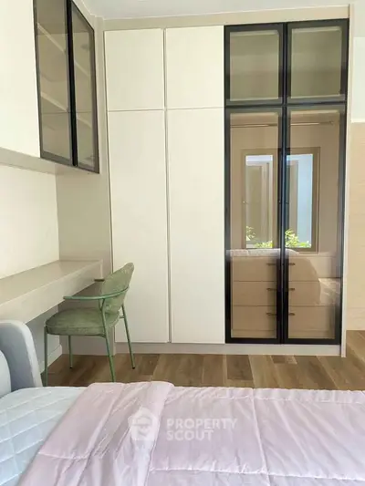Modern bedroom with sleek wardrobe and cozy workspace, featuring elegant design and natural light.