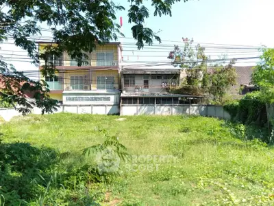 Spacious green plot with potential for development, featuring a two-story building in a serene neighborhood.