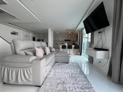 Luxurious modern living room with sleek design and open kitchen layout, featuring plush seating and a wall-mounted TV.