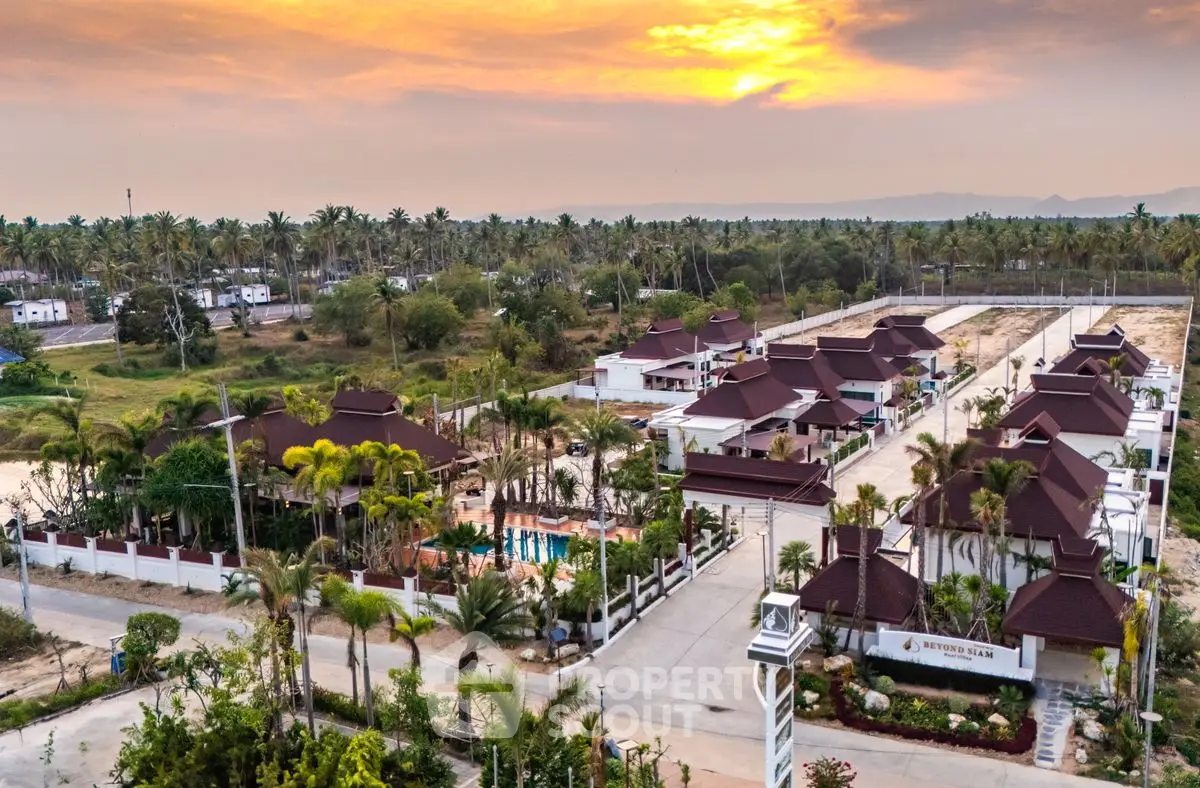 Stunning aerial view of a luxurious tropical villa community at sunset, surrounded by lush greenery and palm trees.