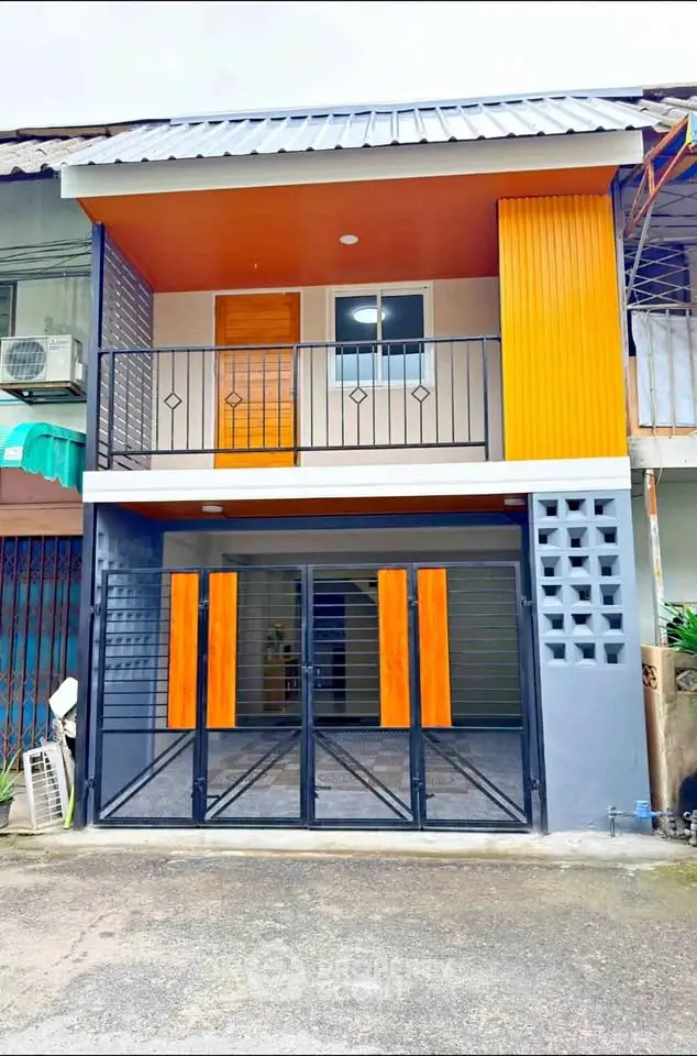 Modern two-story townhouse with vibrant orange accents and gated entrance.