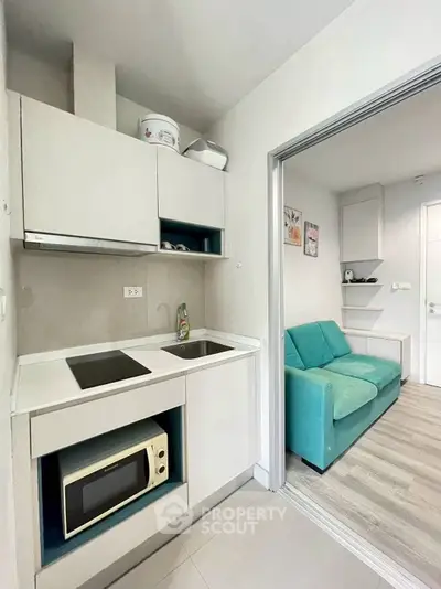 Modern compact kitchen with microwave and induction stove, adjacent to cozy living area with teal sofa.