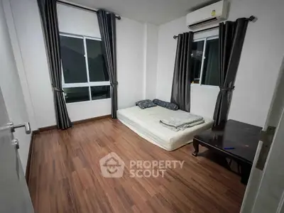 Minimalist bedroom with wooden flooring and large windows for natural light.