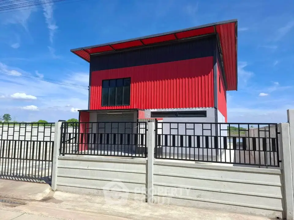 Modern red and gray industrial-style building with a sleek metal roof and fenced perimeter.