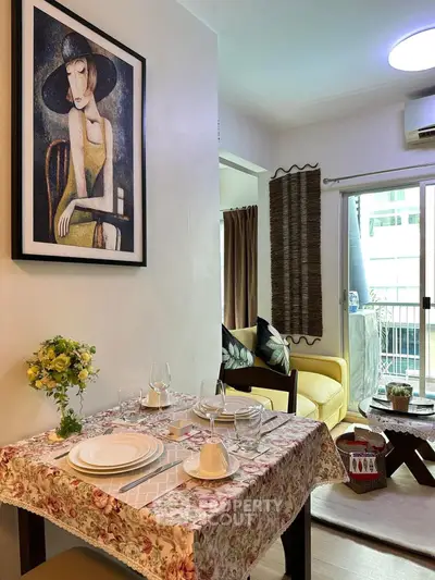 Charming dining area with floral tablecloth and art, leading to cozy living room and balcony.