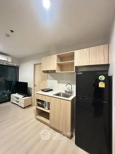 Modern compact kitchen with sleek black fridge and wooden cabinetry in a stylish apartment.