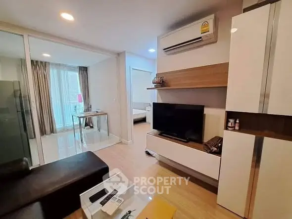Modern living room with sleek furniture and large TV, adjacent to a bright bedroom.