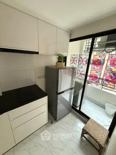 Modern kitchen with sleek cabinets and large fridge, featuring vibrant stained glass window accents.