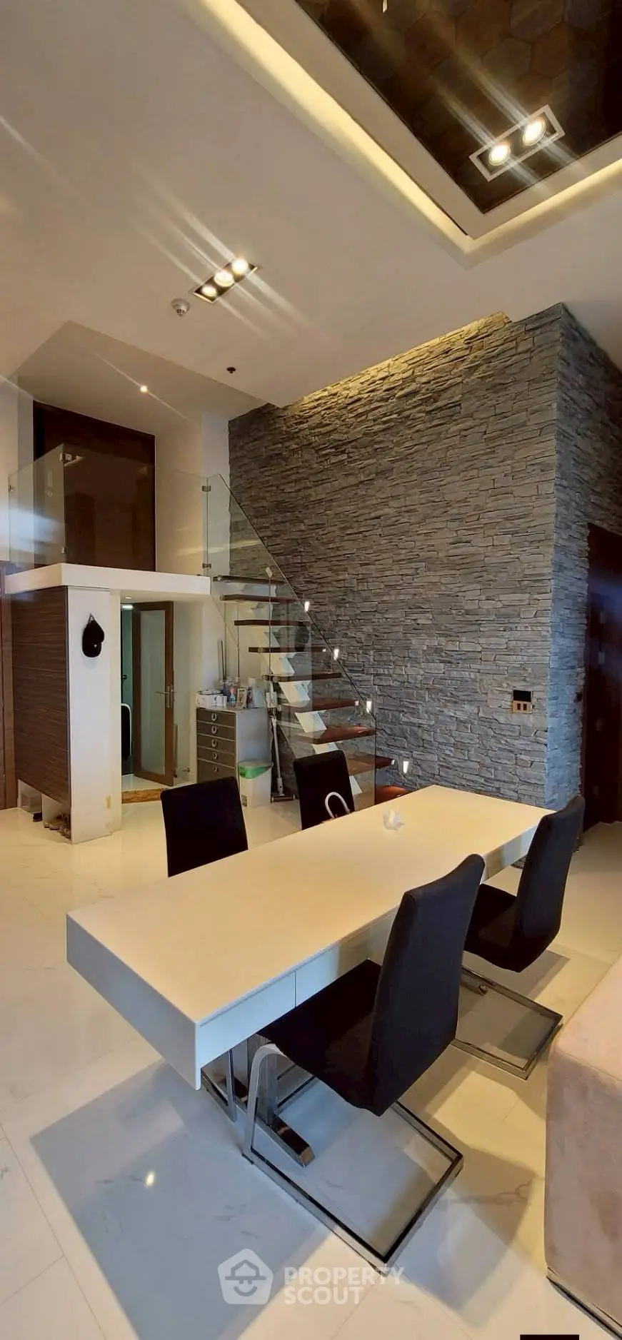 Modern dining area with sleek table and chairs, stone accent wall, and stylish staircase