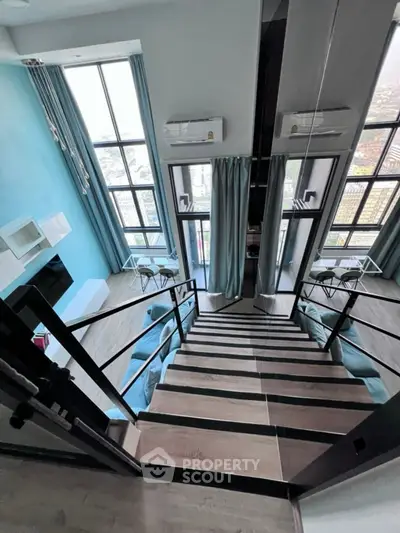 Modern duplex apartment with stylish staircase and large windows offering city views.