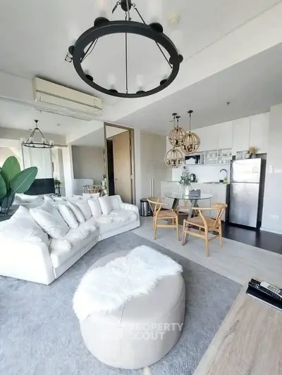 Modern open-layout living room with stylish decor and kitchen area, featuring cozy seating and contemporary lighting.
