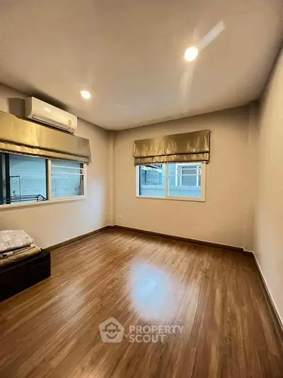 Spacious empty bedroom with wooden flooring and large windows for natural light.