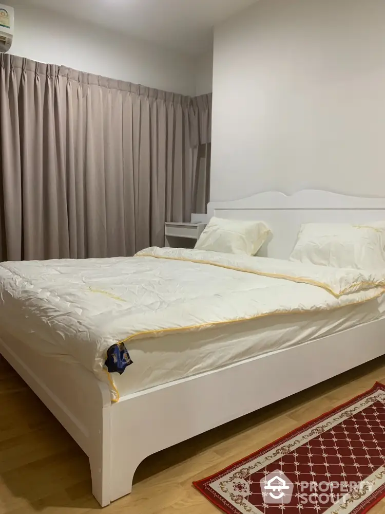 Cozy bedroom with elegant white bed and plush bedding, featuring warm wooden flooring and soft lighting for relaxation.