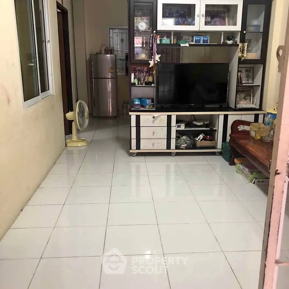 Cozy living room with tiled floor, TV unit, and refrigerator, perfect for modern living.