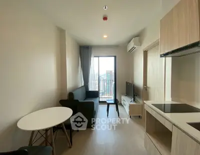 Modern living room with balcony view, sleek furniture, and open kitchen layout.