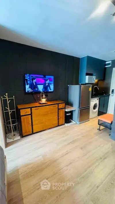 Modern studio apartment with sleek kitchen and cozy living area, featuring a TV and washing machine.