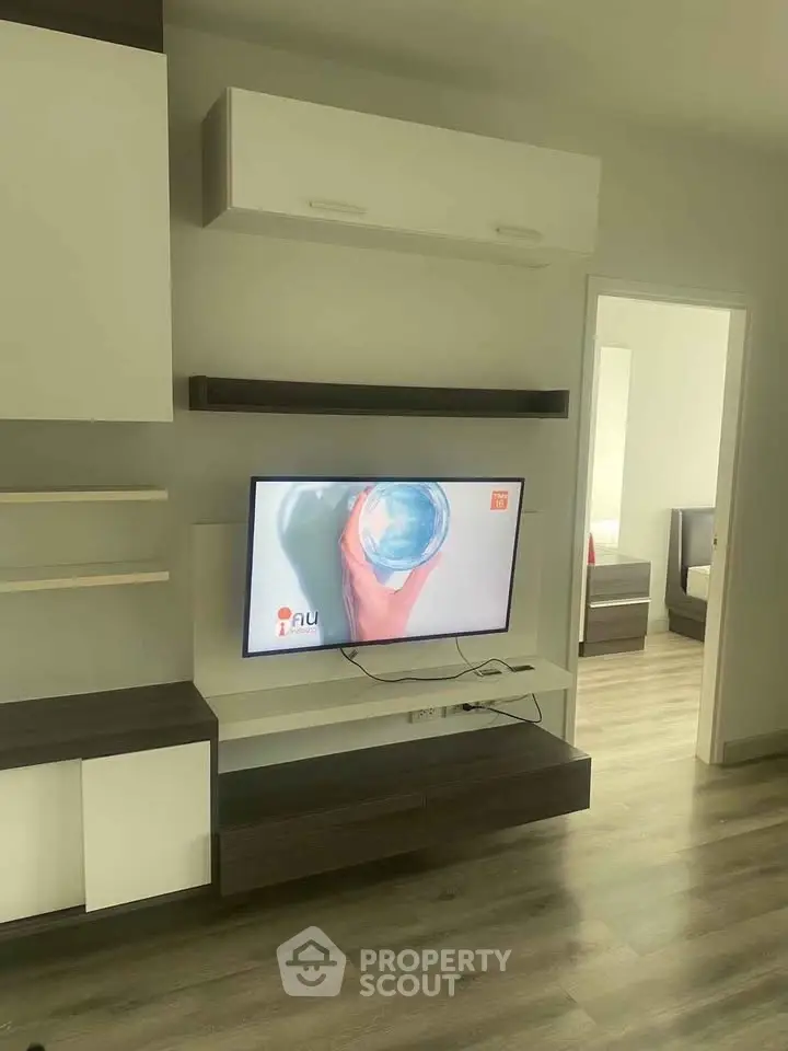 Modern living room with sleek TV unit and open doorway to bedroom, showcasing contemporary design.