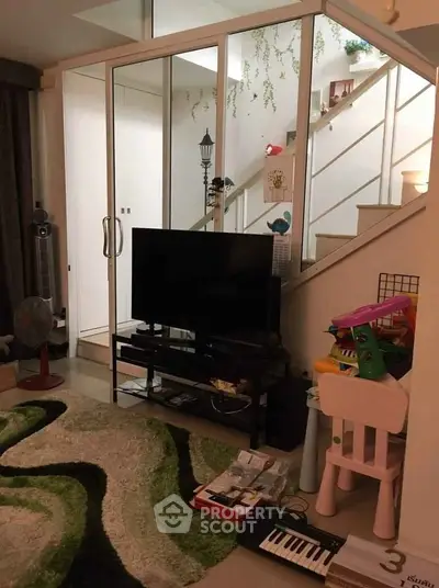 Modern living room with stylish decor and staircase, featuring a TV and playful children's area.