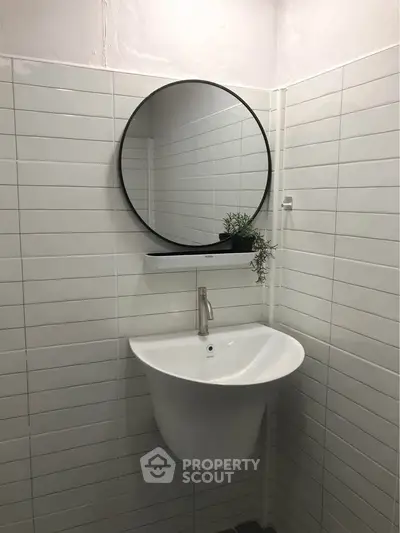 Modern minimalist bathroom with round mirror and sleek white sink.