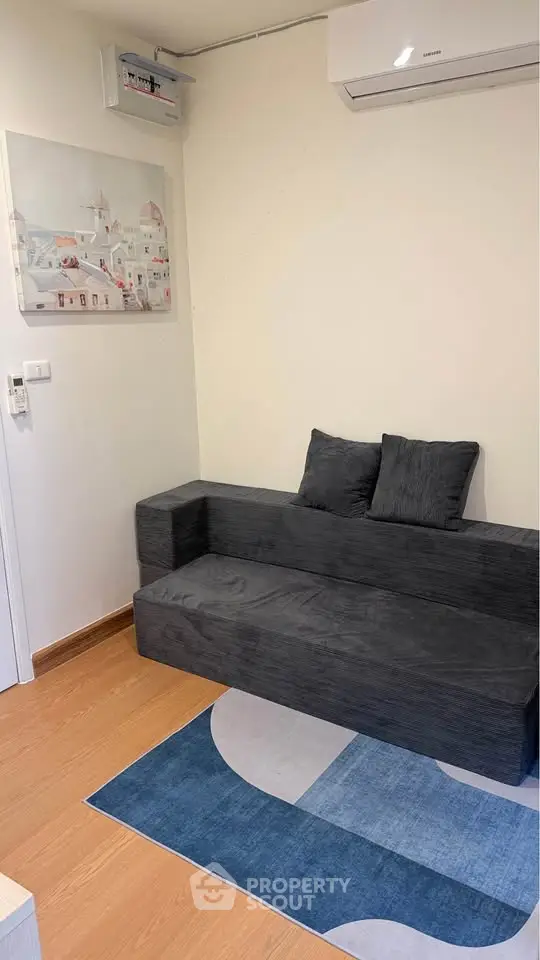 Cozy living room with modern sofa and wall art, featuring air conditioning and wooden flooring.