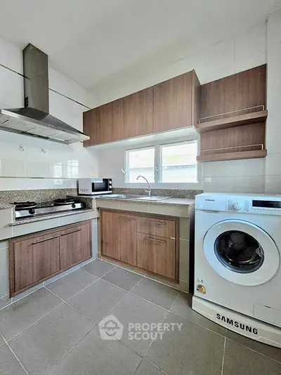 Modern kitchen with gas stove, microwave, and washing machine in sleek design.