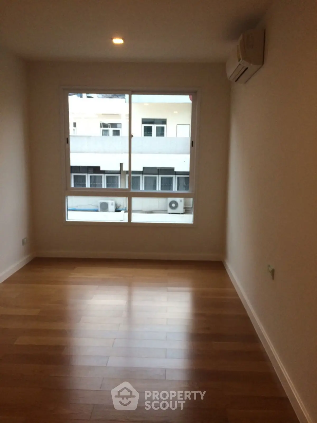 Spacious empty room with wooden flooring and large window view.