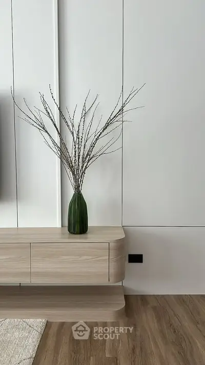 Modern minimalist interior with sleek wooden console and elegant vase on hardwood floor.