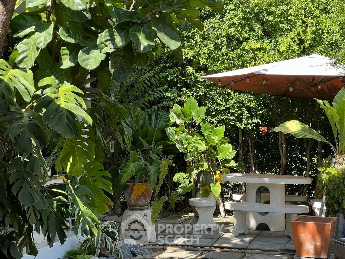 Charming garden patio with lush greenery and shaded seating area, perfect for outdoor relaxation.