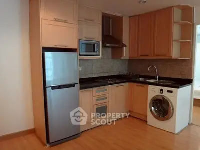 Modern kitchen with wooden cabinets, stainless steel fridge, microwave, and washing machine.