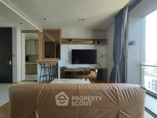 Modern living room with leather sofa and large TV, featuring open layout and balcony view.