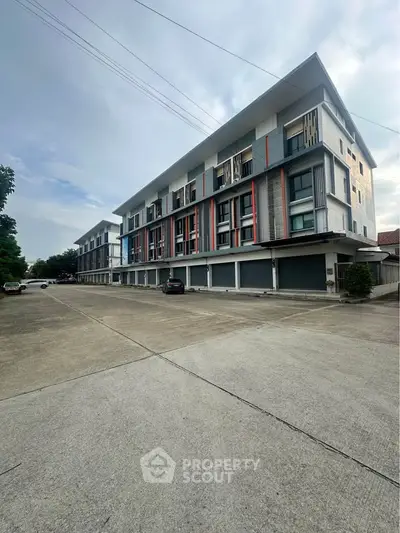 Modern multi-story building with sleek design and spacious parking area, ideal for urban living.