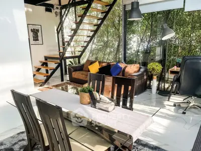 Modern living room with glass walls, stylish staircase, and elegant dining area.