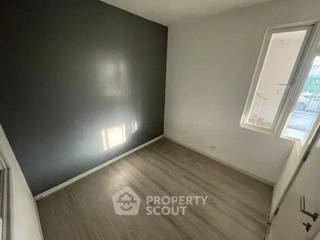 Minimalist small room with wooden flooring and a dark accent wall, perfect for creative design.