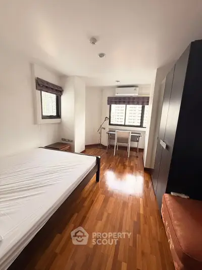 Spacious bedroom with wooden flooring and natural light in modern apartment