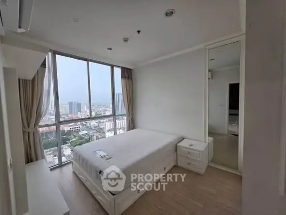 Spacious bedroom with large window offering stunning city views in modern apartment.