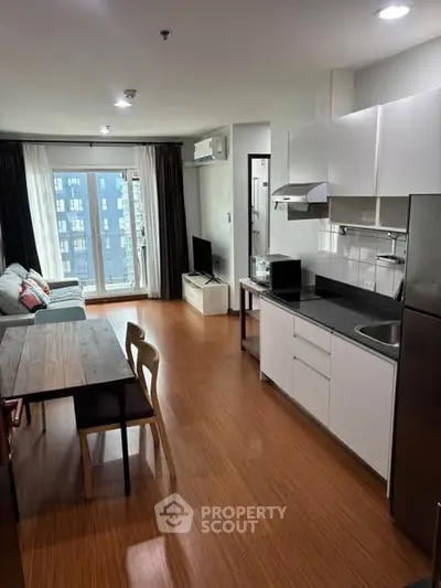 Modern open-layout kitchen and living room with wooden flooring and natural light.