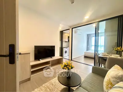 Modern open-plan living room with TV, dining area, and view into bedroom, featuring stylish decor and natural light.